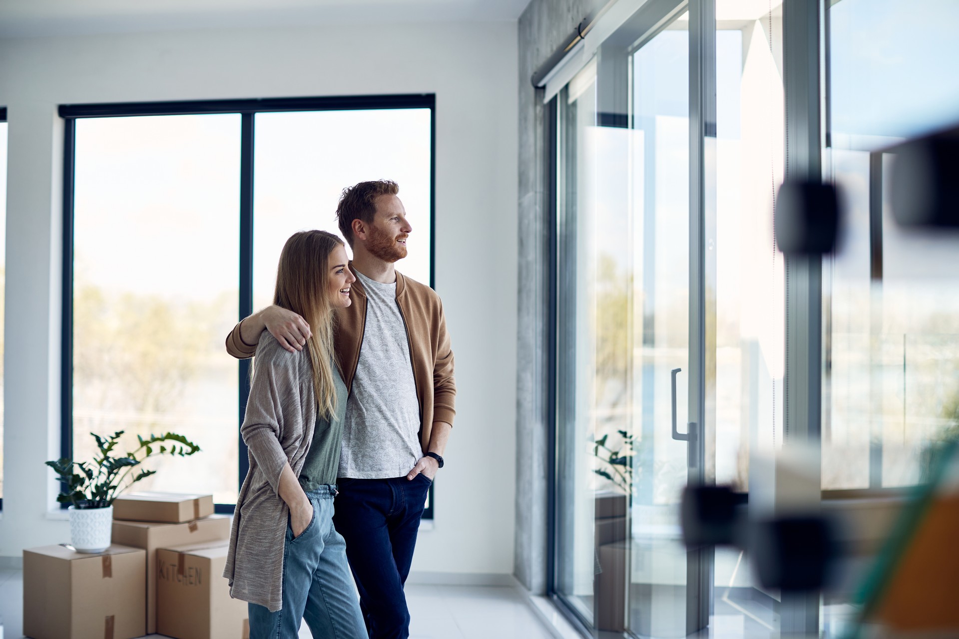 Young embraced couple looking through the window of their new apartment.