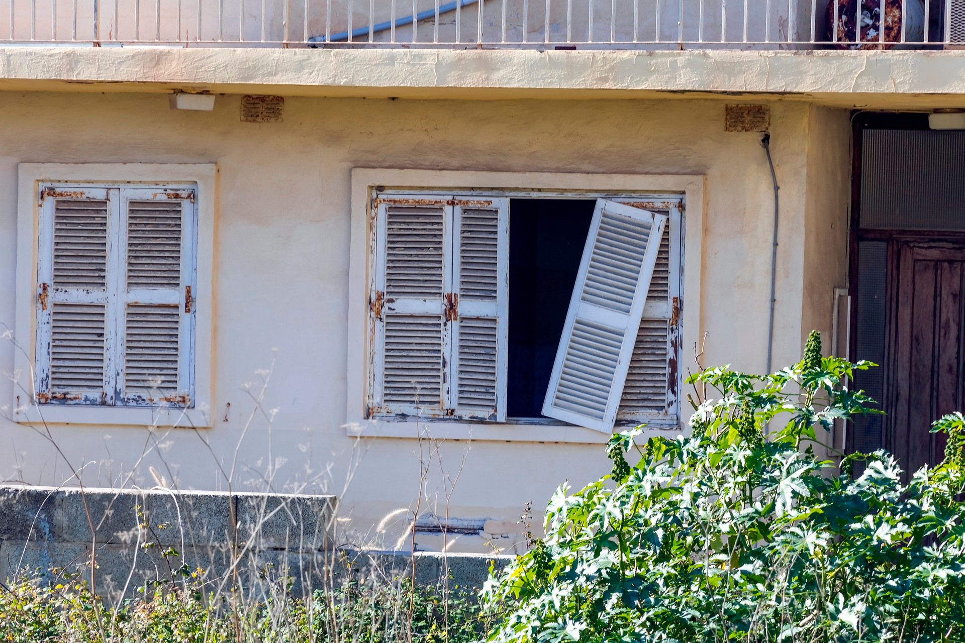 Detail of abandoned grunge yellow stone rural house with broken window and cactus growing in the garden